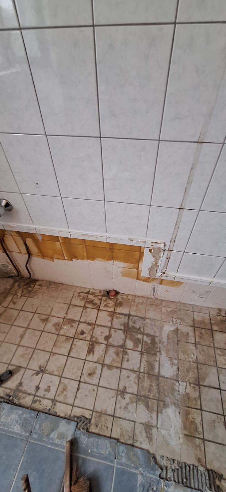 Badkamerrenovatie in uitvoering: verwijderde tegels in een badkamer met wit-grijze bloktegels.